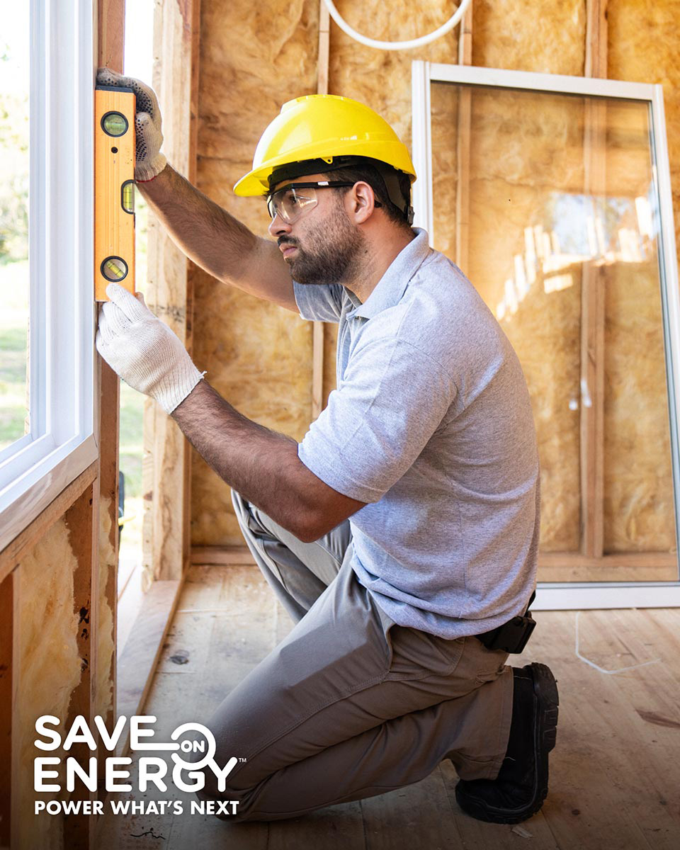 A man in a yellow hard hat uses a level to check a window on a construction site